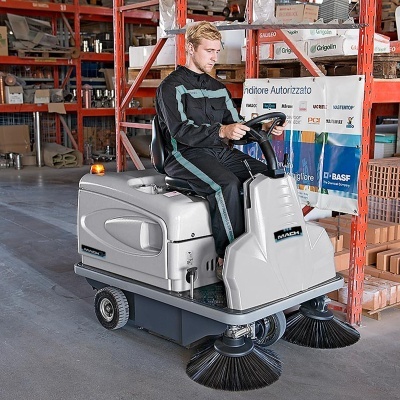 Máquina de limpeza industrial com escovas e condutor num armazém