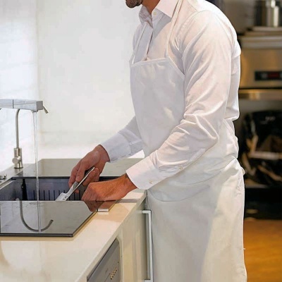 Homem a preparar comida numa cozinha, veste camisa e avental brancos