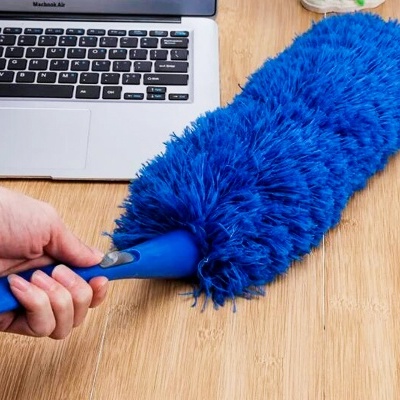 Poeira azul com cabo azul segurado sobre mesa de madeira clara ao lado de laptop