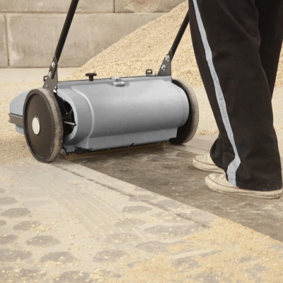 Máquina manual cinzenta para limpeza de sementes com rodas pretas e pega, usada por pessoa com calças pretas e risca branca