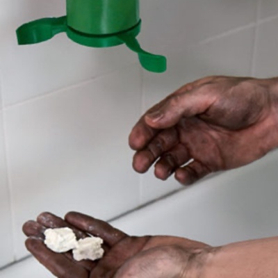 Mãos sujas com pedaços brancos sob dispensador verde na parede