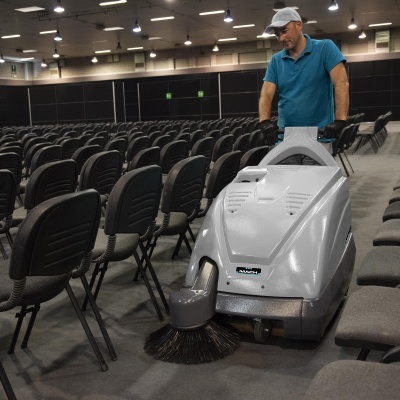 Homem a operar máquina de limpeza cinzenta numa sala com muitas cadeiras pretas e cinzentas