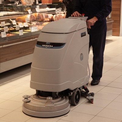 Máquina de limpeza industrial cinzenta Hako MACH num chão cerâmico claro em loja com expositor de carne