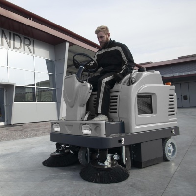 Máquina varredora industrial cinza ao ar livre com operador em roupa preta