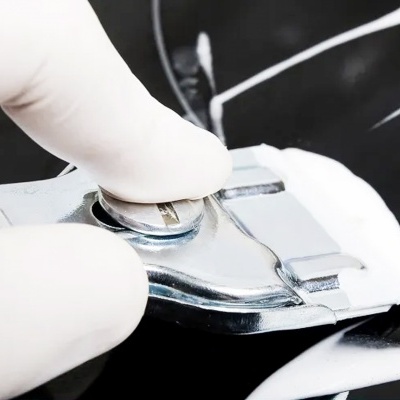 Máquina de barbear metálica com lâmina, mão com luva branca e espuma