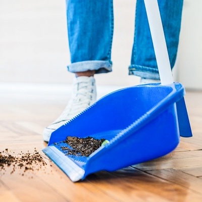 Pessoa a varrer terra para uma pá de lixo azul num chão de madeira clara