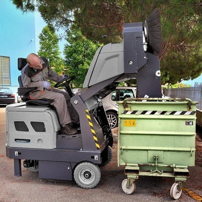 Máquina industrial de limpeza com escova circular junto a contentor verde ao ar livre