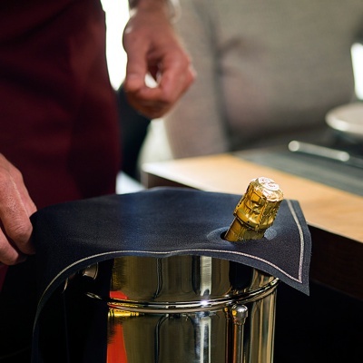 Frasco de champanhe dourado coberto por pano preto numa tina metálica.