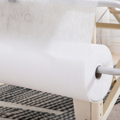 Rolo de tecido branco em suporte de madeira numa sala com tapete geométrico