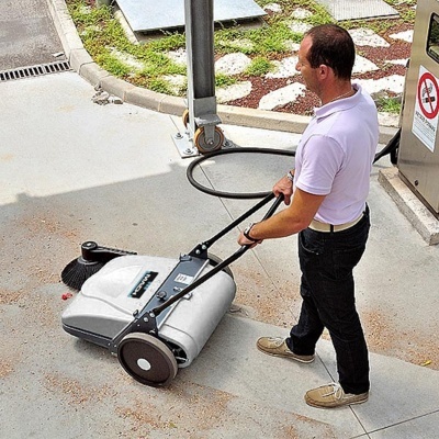 Homem a usar uma varredeira manual cinza num piso exterior cinzento