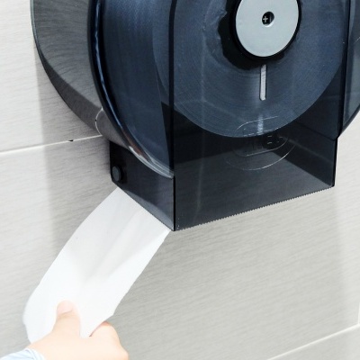 Dispenser de papel higiénico preto numa parede com mão a puxar papel branco