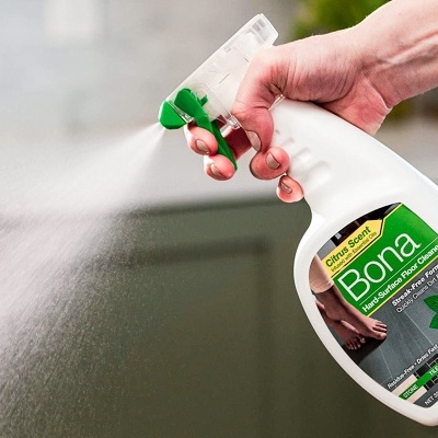 Frasco de spray para limpeza Bona com rótulo verde e preto e mão a disparar spray.