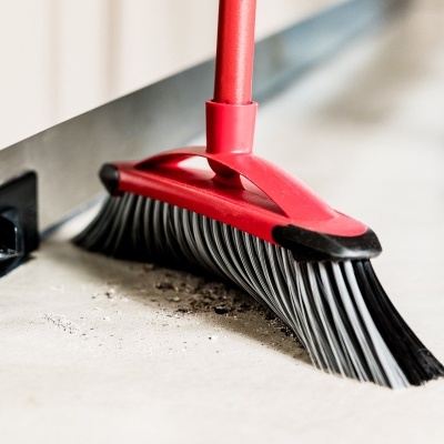 Vassoura vermelha a varrer pó perto de tomada com etiqueta ALDEN