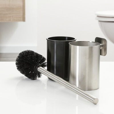 Escova sanitária com suporte metálico prateado e preto em superfície branca próximo a sanita