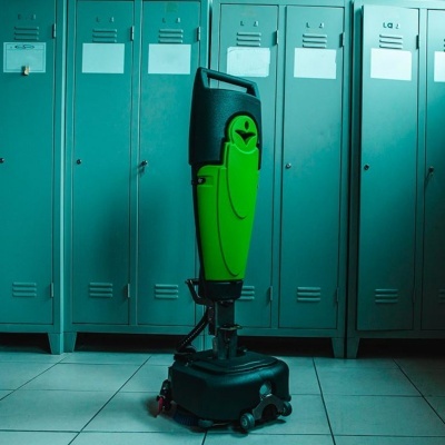 Equipamento de limpeza verde e preto com rodas, em frente a armários metálicos azuis