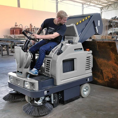 Máquina de limpeza industrial cinzenta com escovas frontais redondas pretas e operador