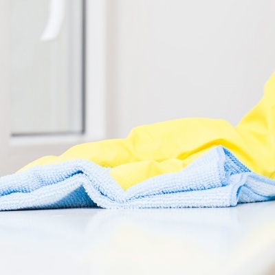 Mão com luva amarela a limpar superfície branca com pano azul