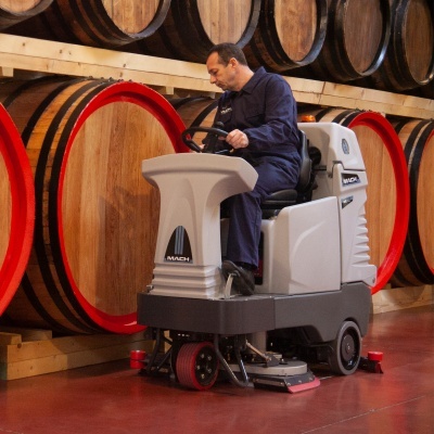 Homem numa máquina de limpeza industrial junto a barris de madeira em armazém