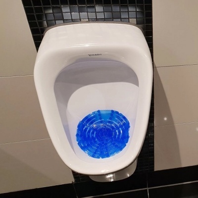 mictório branco com disco azul no interior numa parede com azulejos