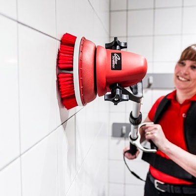 Mulher a usar escova elétrica vermelha com cabo para limpeza de parede de azulejos brancos