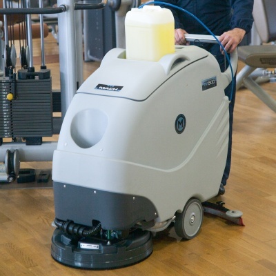 Máquina de limpeza floor scrubber cinzenta com depósito amarelo num ginásio