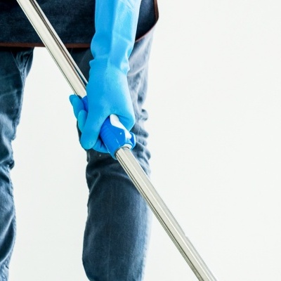 Pessoa com luvas azuis segurando cabo metálico de esfregona