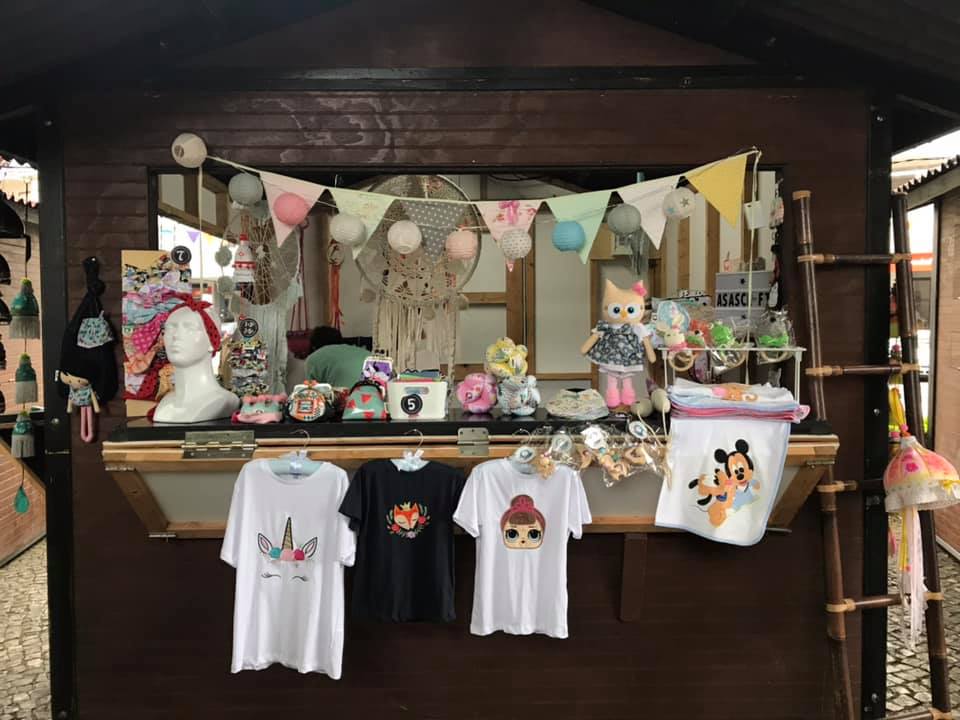 Banca de madeira com t-shirts estampadas e artigos de decoração em feira ao ar livre.