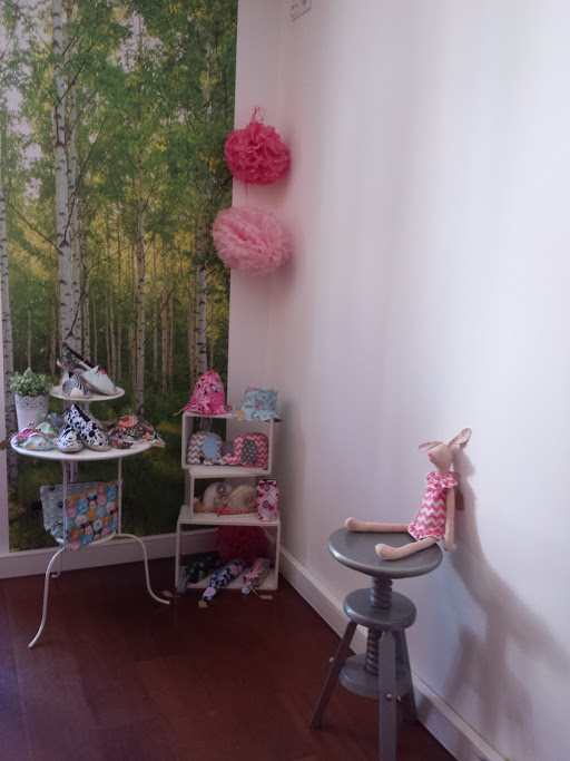 SPA Day Sapatos de criança coloridos expostos numa mesa e prateleira junto a parede com papel de parede de floresta e cadeira com boneca de tecido.