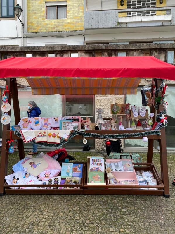 Banca de mercado com toldo vermelho a vender itens de artesanato e produtos infantis
