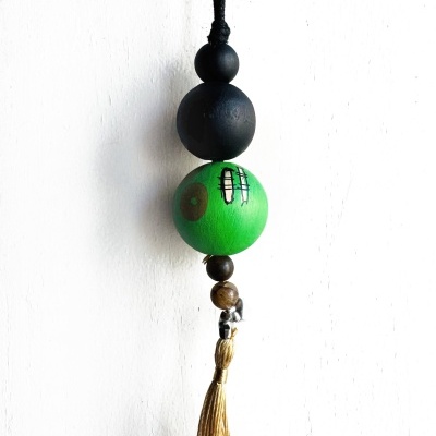 Chaveiro artesanal com bolas de madeira preta e verde e tassel dourado suspenso numa parede branca