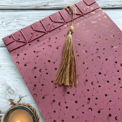Caderno rosa com padrão dourado de constelações e tassel dourado