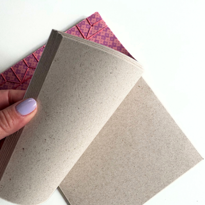 Dois cadernos em papel reciclado, um com capa rosa padrão e costura vermelha, páginas cinza claro
