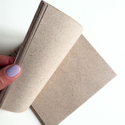 Folhas de papel reciclado castanho claro sendo seguradas por mão com unha lilás