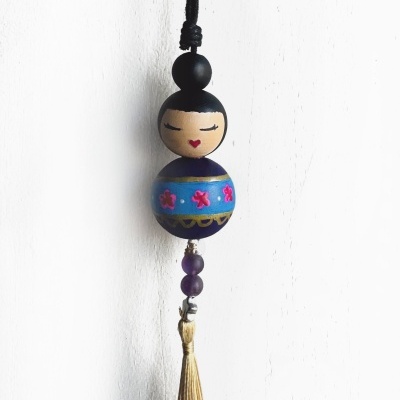 Pendente decorativo em madeira com figura feminina azul, rosa e dourada, com franja dourada.