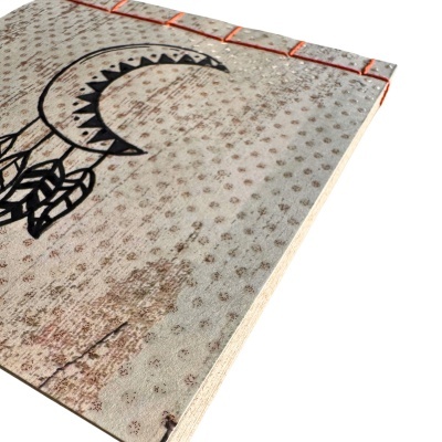 Livro com capa dura clara e desenho preto de meia-lua e penas com costura alaranjada