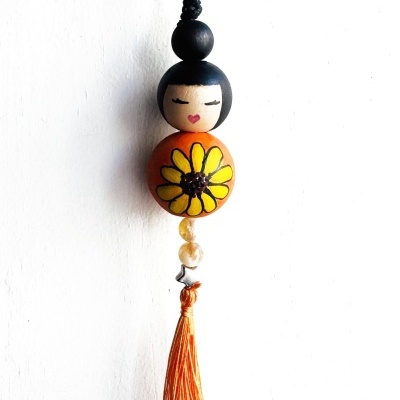 Chaveiro de madeira com boneca, flor amarela e tassel laranja