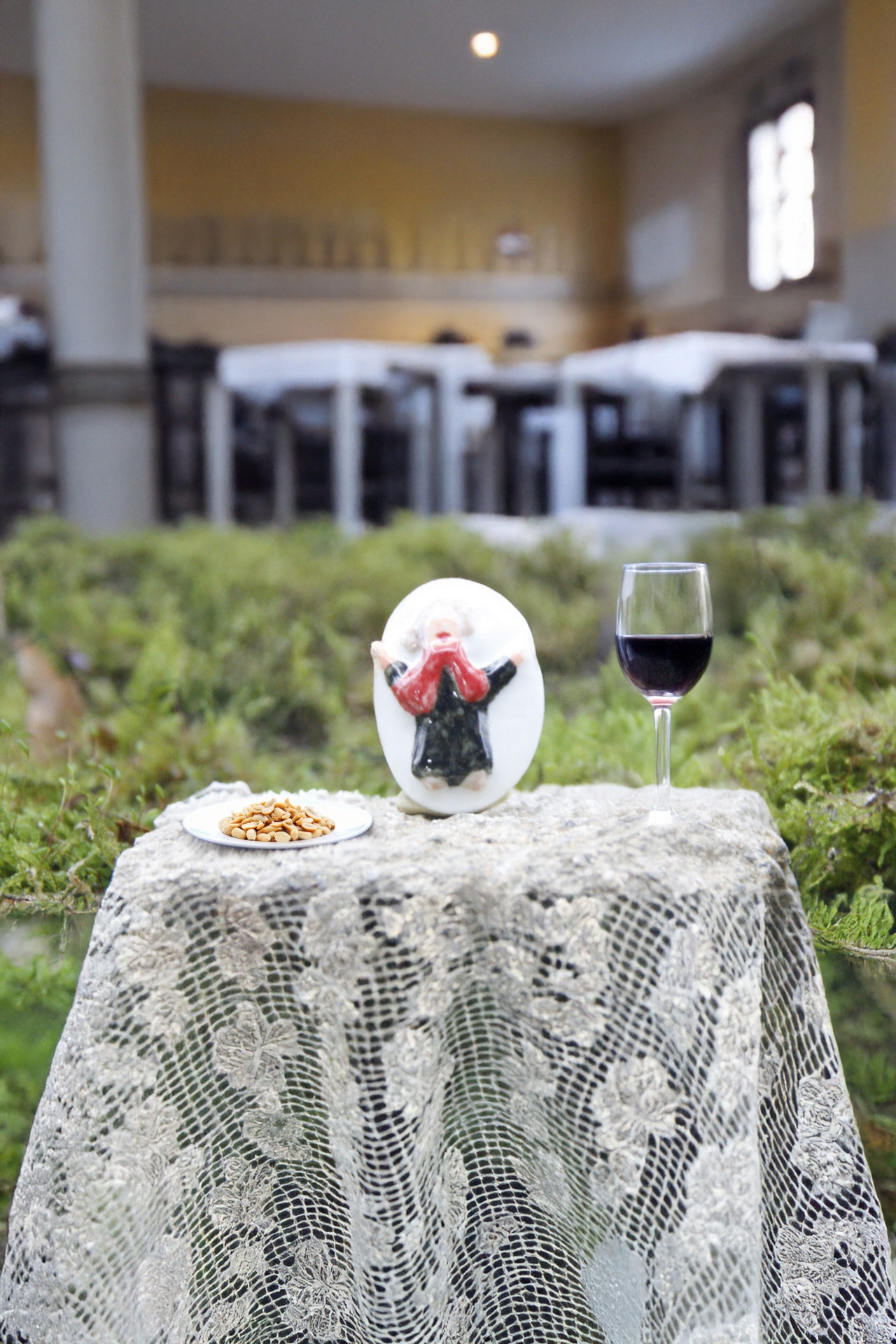 Fadista Mesa pequena com toalha rendada, prato com frutos secos, taça de vinho tinto e peça decorativa oval em ambiente interno