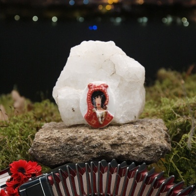 Acordeão preto e vermelho com pedras e enfeite colorido em primeiro plano, fundo noturno desfocado