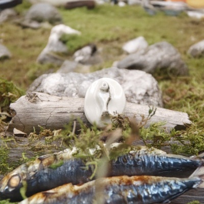 Peixes grelhados sobre musgo com prato branco e barcos ao fundo ao ar livre