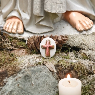 Pés nus de estátua branca com tecido, anel branco com cruz vermelha, candelabro aceso, musgo e pinhas