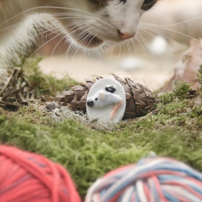 Gato a olhar para figura de rato no meio de musgo com novelos de lã à frente