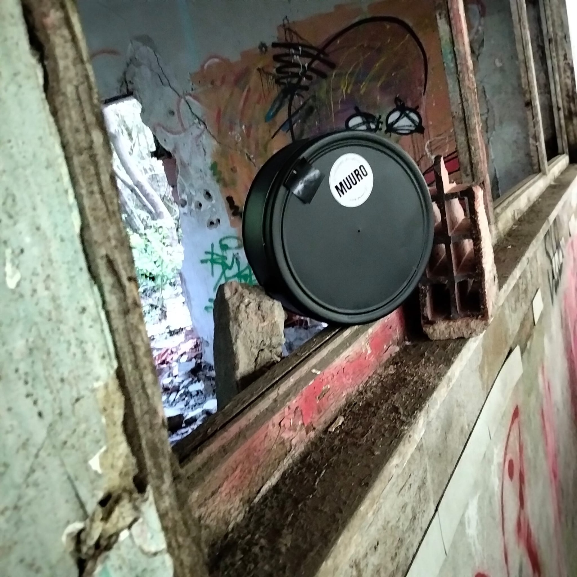 Frasco preto redondo com etiqueta MUURO numa janela velha e parede grafitada