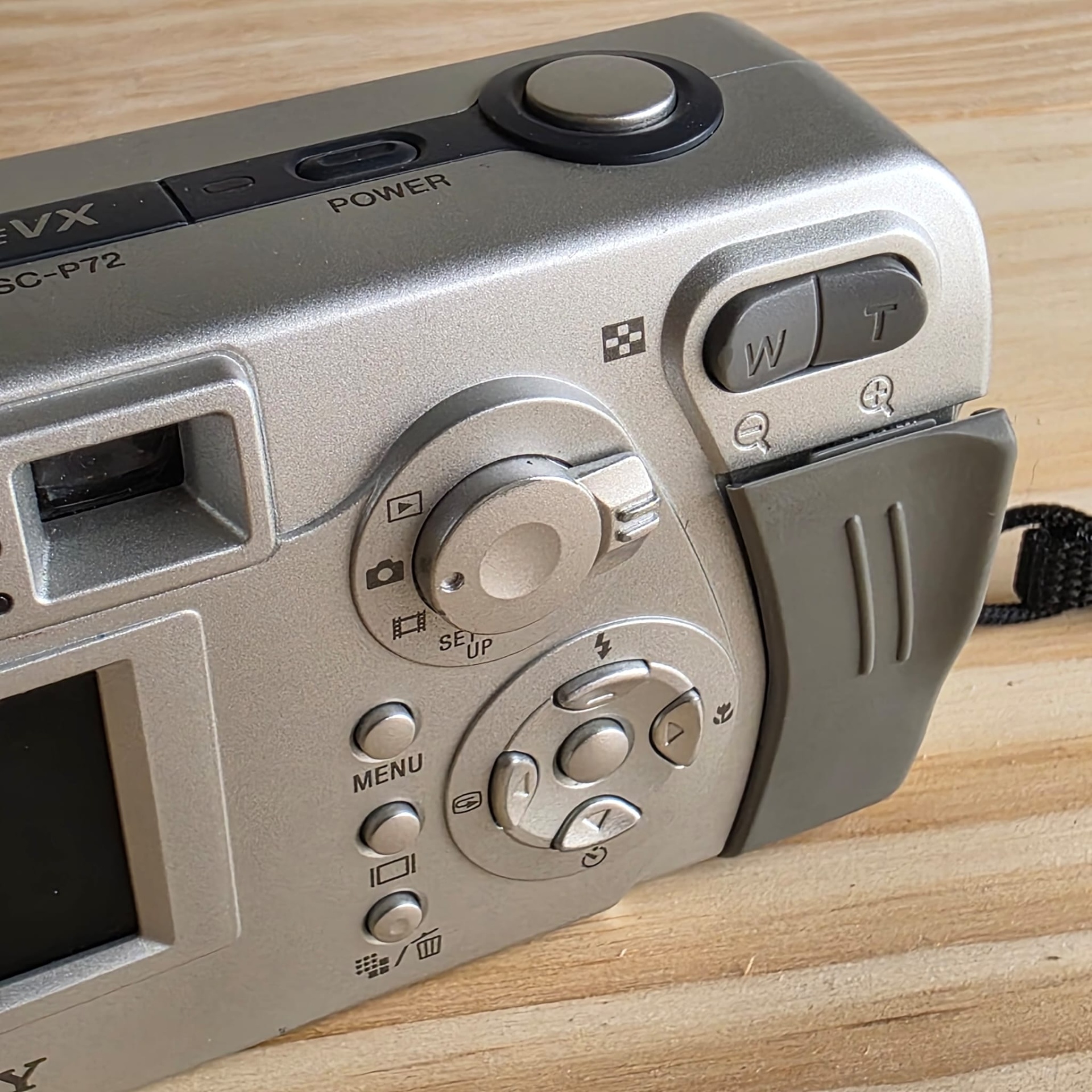 Sony Cyber Shot 3,2 Câmara digital prateada com botões e controlos visíveis sobre mesa de madeira.
