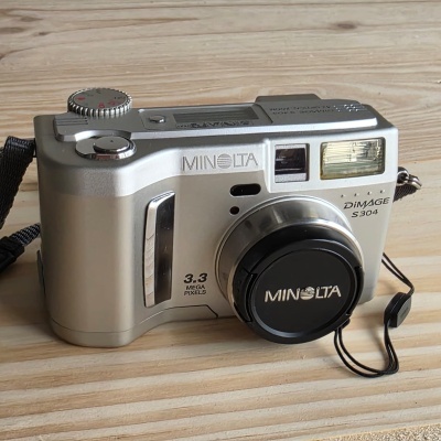 Câmara digital Minolta Dimage S304 prateada sobre madeira clara
