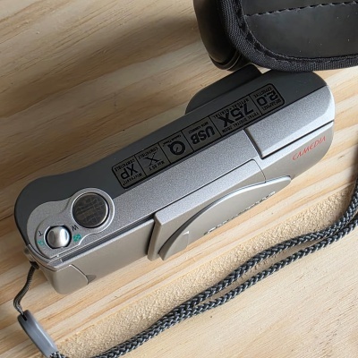 Máquina fotográfica digital prateada Olympus Camedia sobre mesa de madeira clara