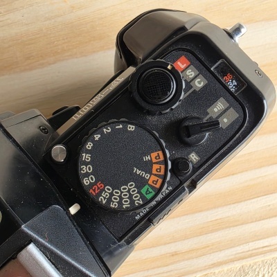 Topo de câmara fotográfica preta com mostrador de velocidades de obturador e botões