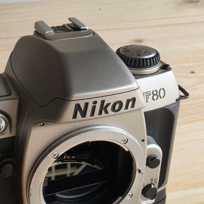 Máquina fotográfica analógica Nikon F80 prateada sobre superfície de madeira