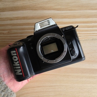 Máquina fotográfica Nikon F-401X analógica preta com flash embutido e botão de seleção sobre madeira.