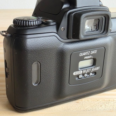 Traseira de uma câmara fotográfica analógica preta com texto QUARTZ DATE PRINT