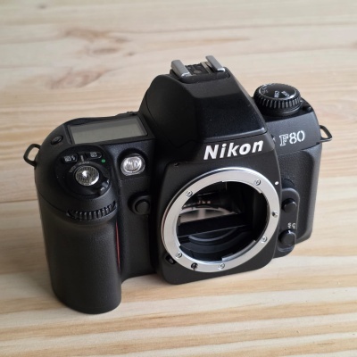Câmara fotográfica Nikon F80 preta sem lente em superfície de madeira
